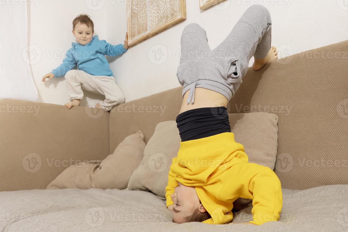 Two active, little kids doing gymnastic handstand exercise in living room. Child standing on hands upside down. Brothers relationship. Children spending time together, having fun during sport. photo