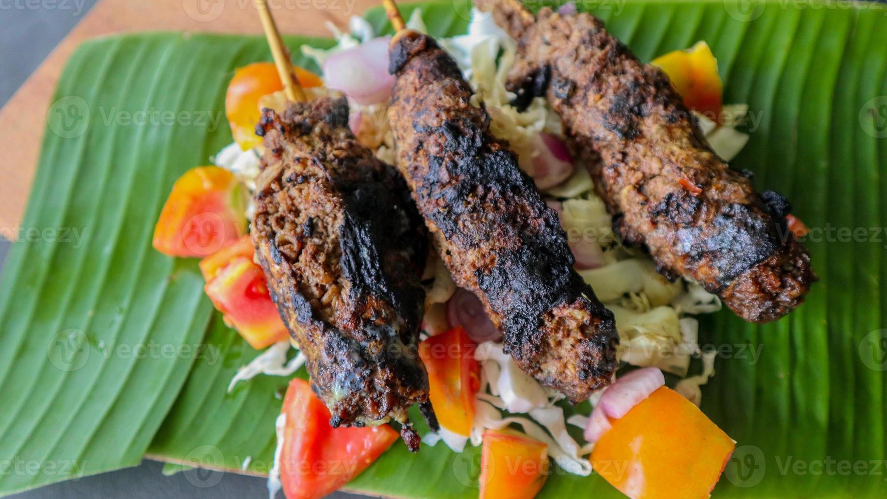 sate buntel or satay buntel is satay made from minced mutton wrapped in mutton fat and then grilled. seasoning with tomatoes, shallots, pepper, cabbage photo