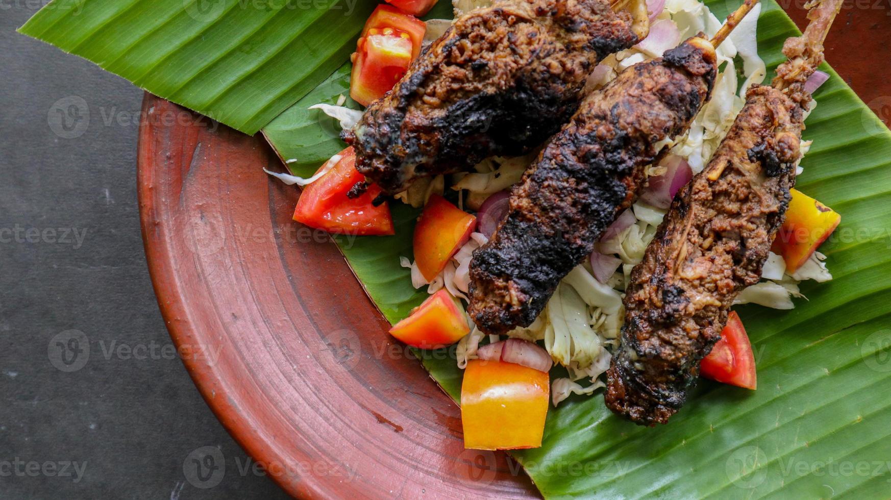 sate buntel o satay buntel es satay hecho de cordero picado envuelto en grasa de cordero y luego asado a la parrilla. condimento con tomates, chalotes, pimienta, repollo foto