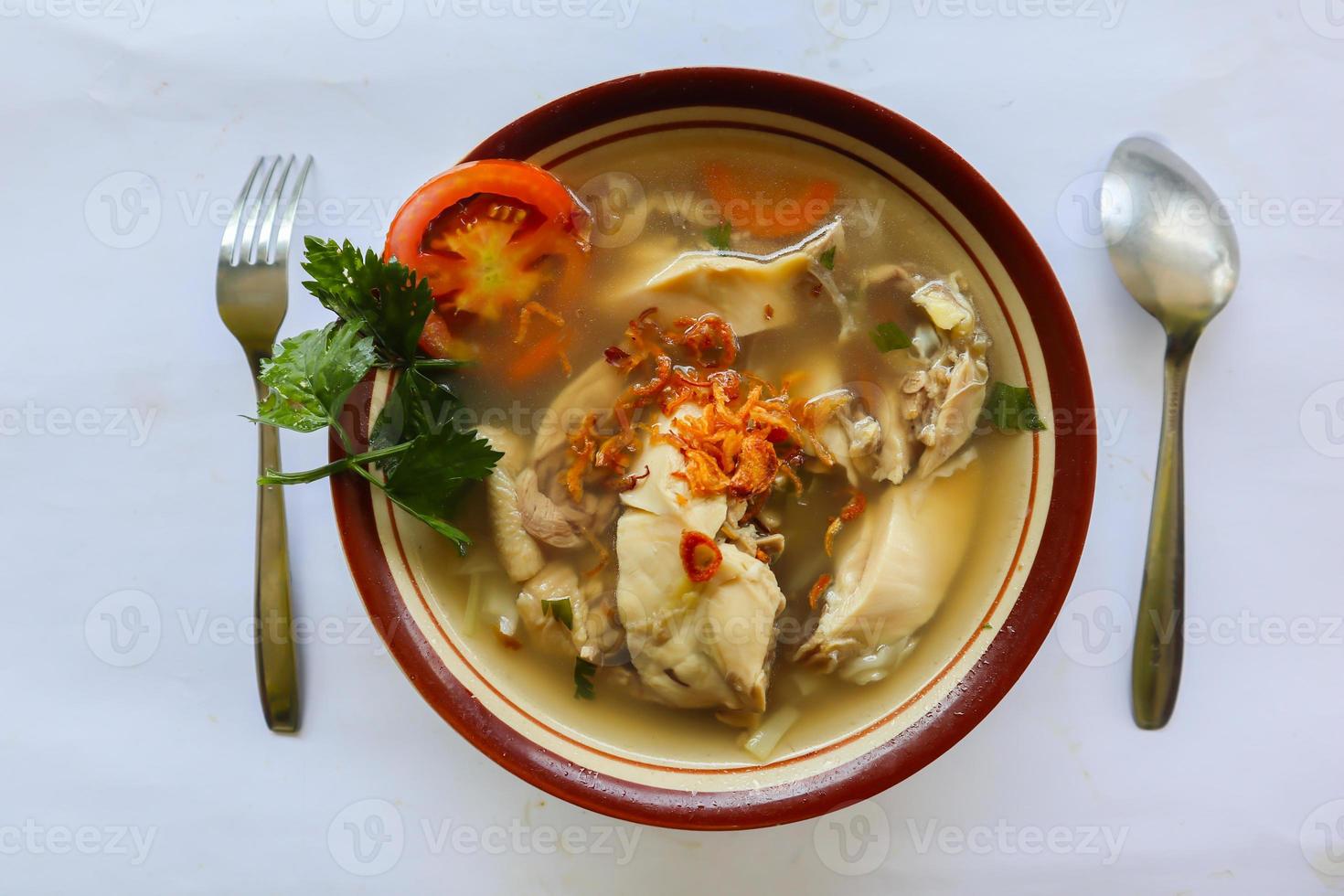 Chicken soup served with vegetables, tomatoes, celery in a bowl, spoon and fork. with black background photo