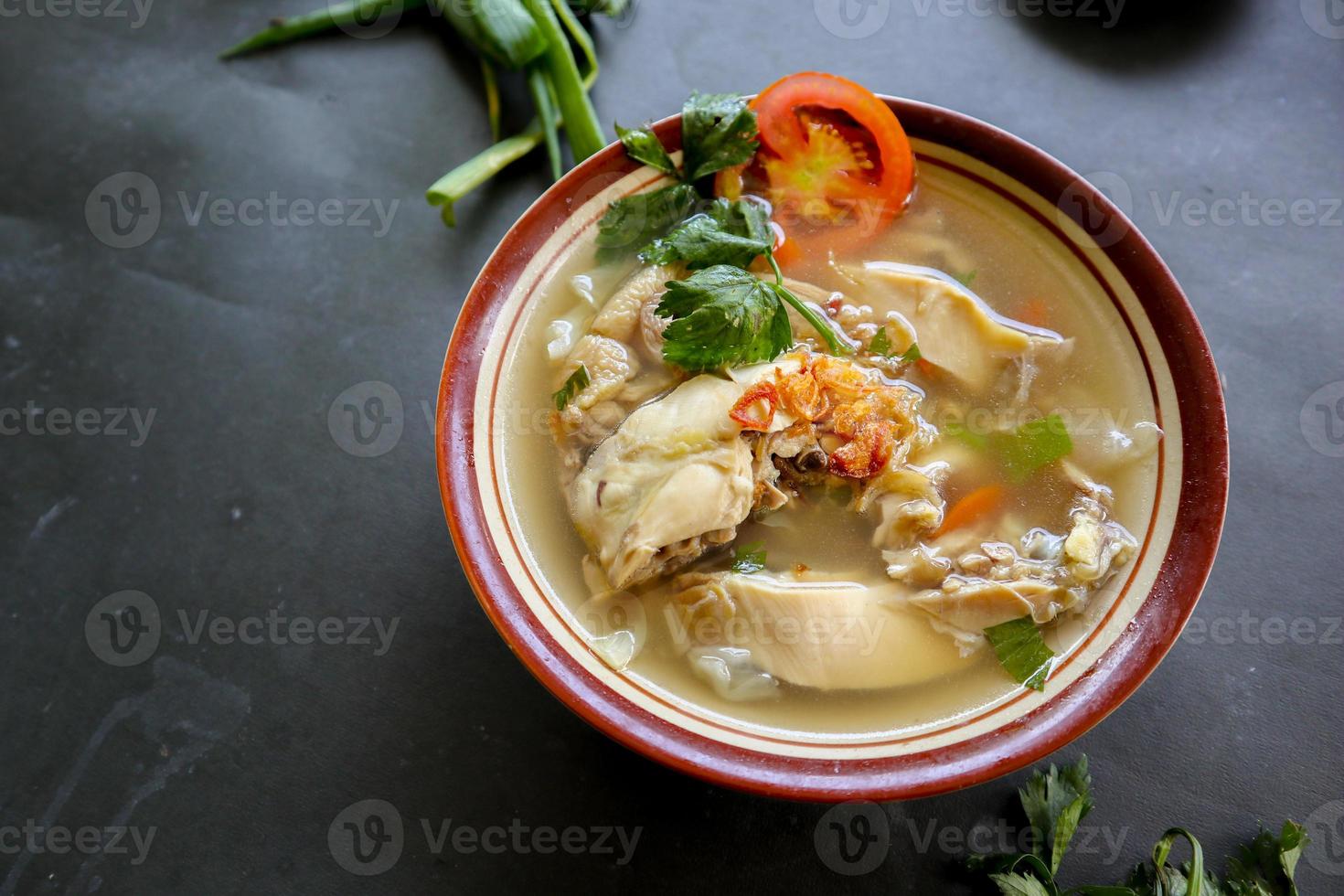 Chicken soup served with vegetables, tomatoes, celery in a bowl, spoon and fork. with black background photo