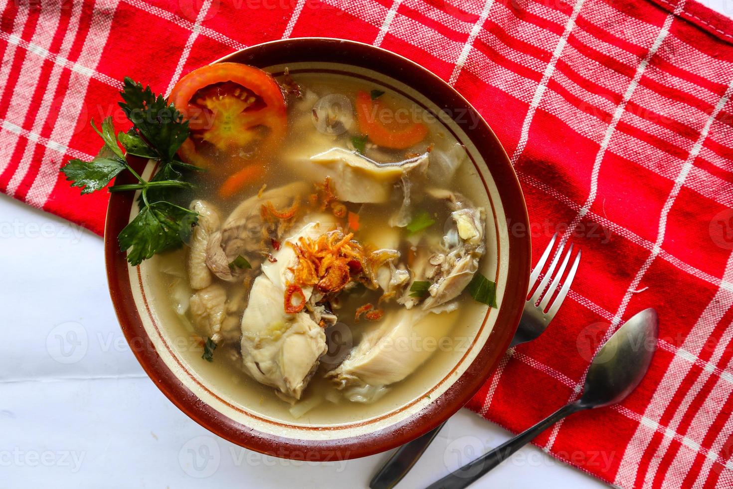 Chicken soup served with vegetables, tomatoes, celery in a bowl, spoon and fork. with black background photo