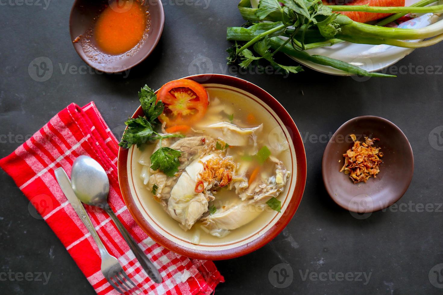 Chicken soup served with vegetables, tomatoes, celery in a bowl, spoon and fork. with black background photo
