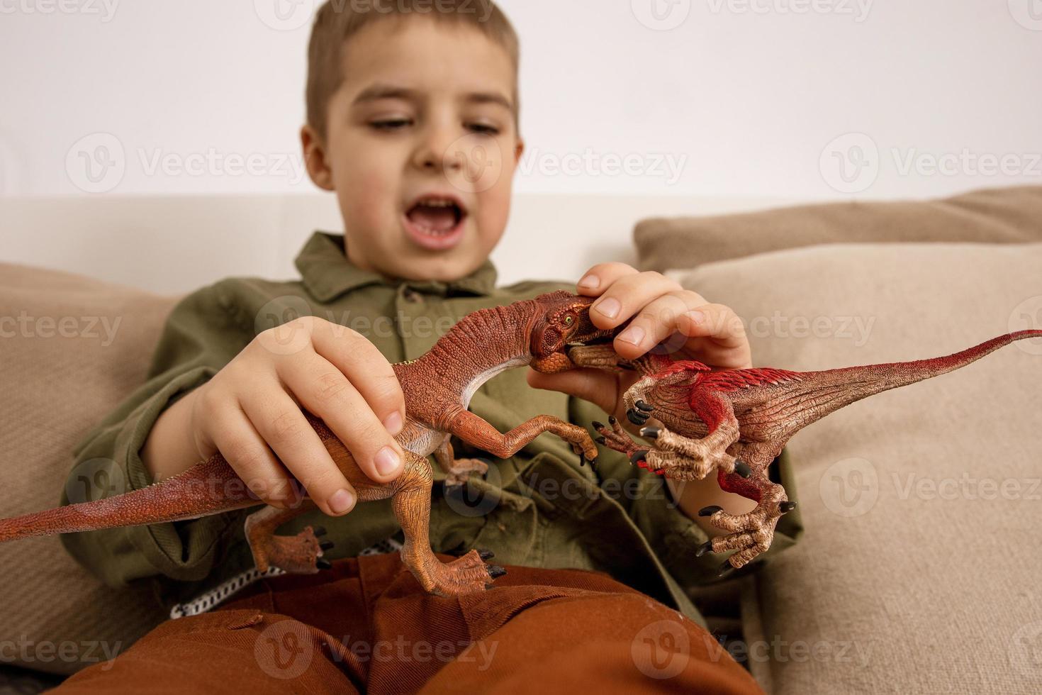 Little and cute caucasian boy playing with dinosaurs at home. Interior and clothes in natural earth colors. Cozy environment. Child having fun with toys. photo