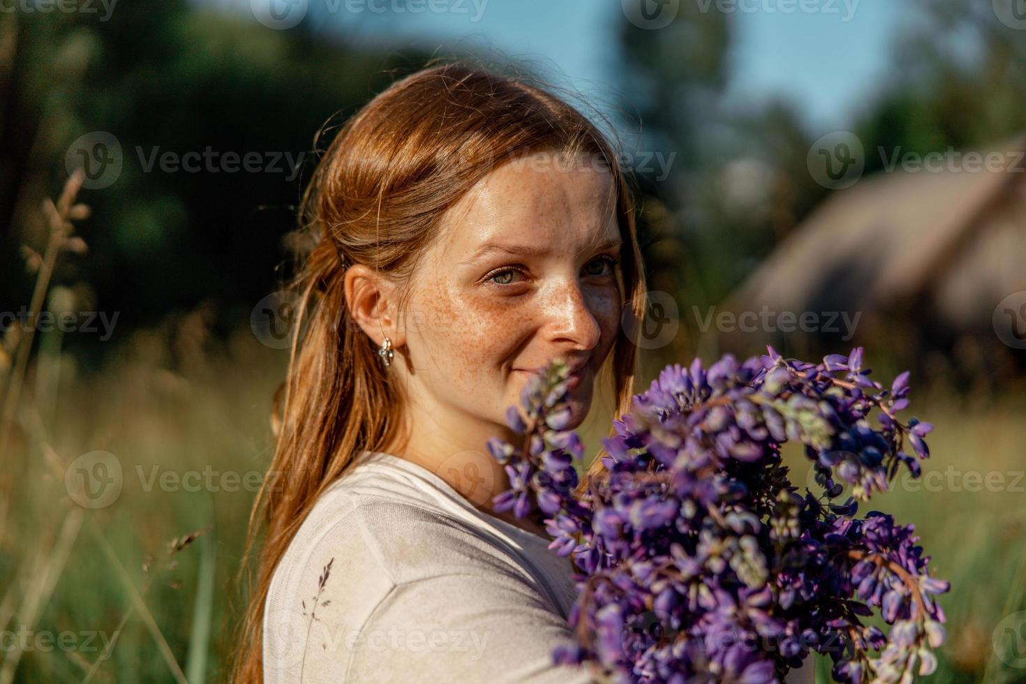 Cierra el retrato de una joven hermosa pelirroja con pecas, vestida de blanco, posando en la naturaleza. chica con cabello rojo sosteniendo flores. belleza natural. diversidad, singularidad individual. foto