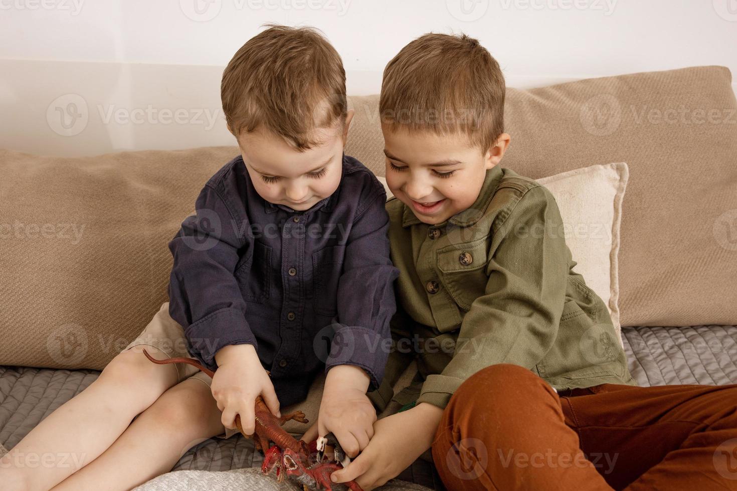 Two little and cute caucasian boys playing with dinosaurs at home. Interior and clothes in natural earth colors. Cozy environment. Children having fun with toys, two friends. photo
