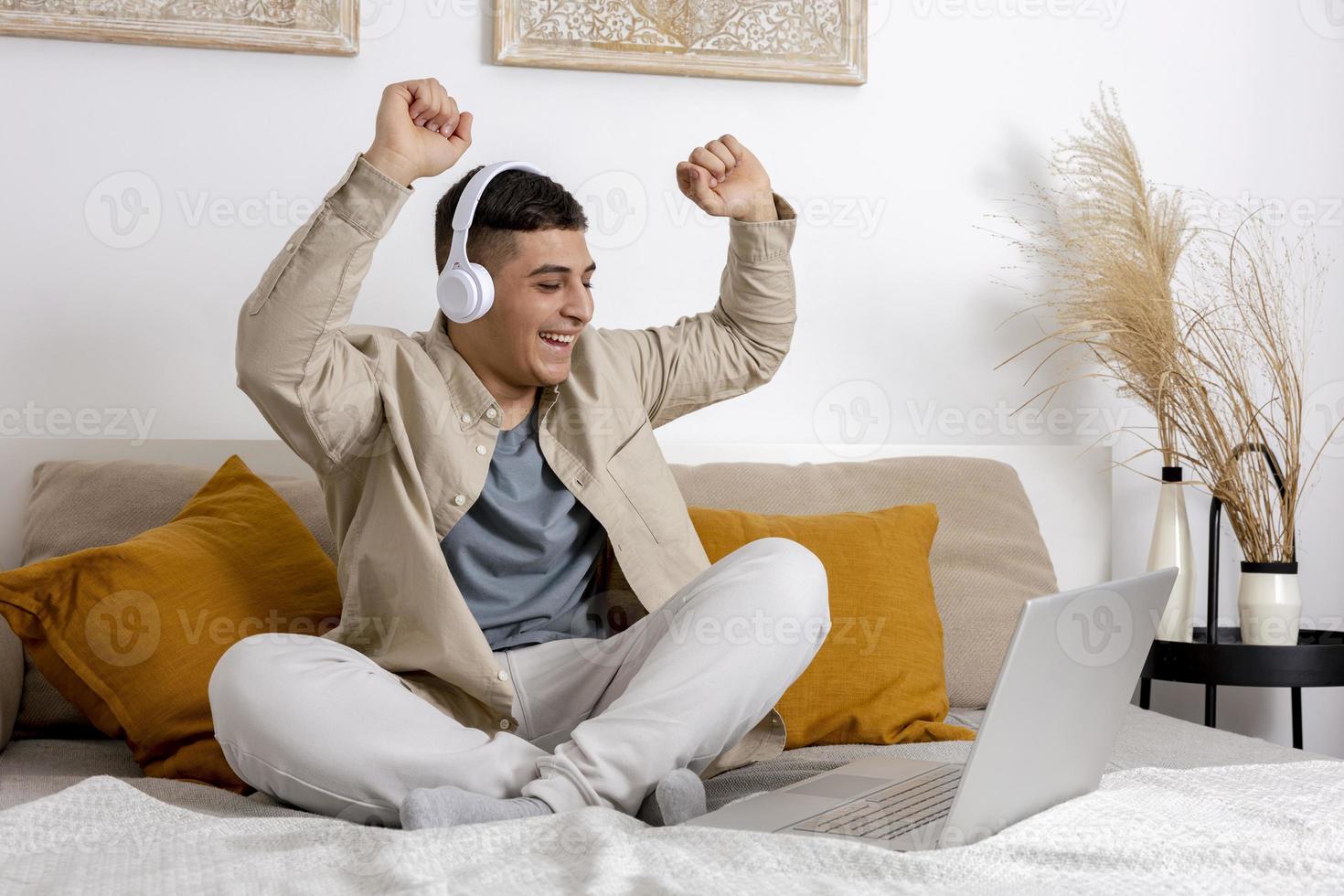 Surprised person, positive emotions. Young man with casual clothes sitting on bed with laptop. Won a prize online. Man using computer to surf in internet, play game, read news, study, call friends. photo