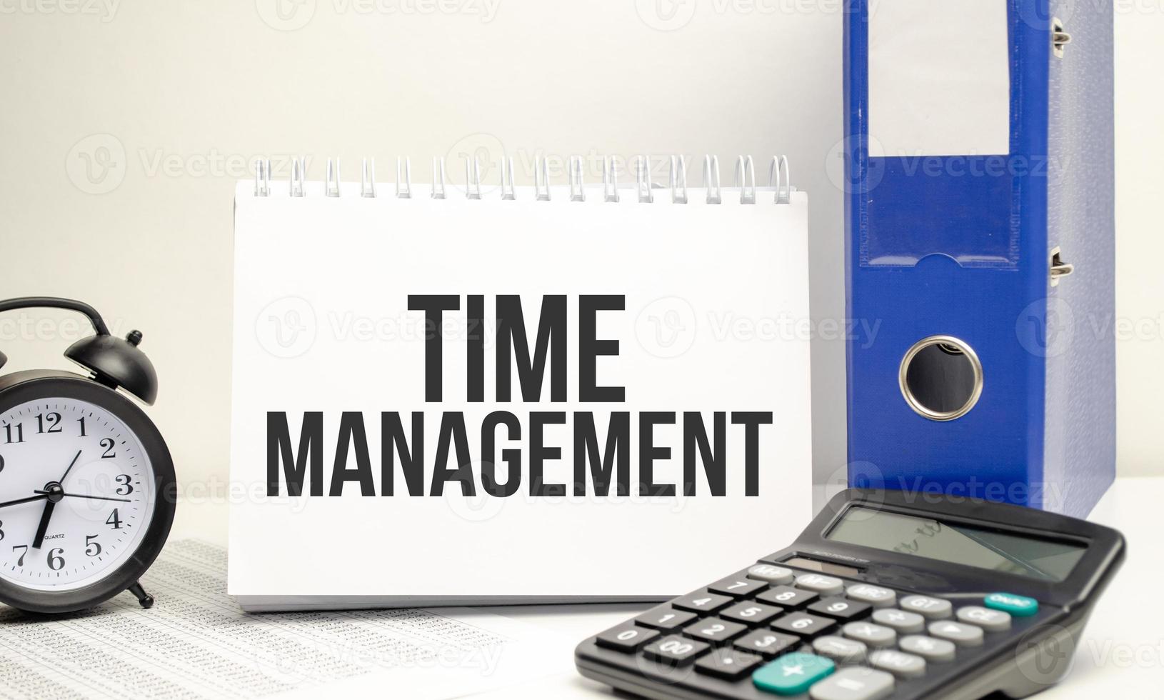 time management words on white notebook with clock, calculator and paper folder photo