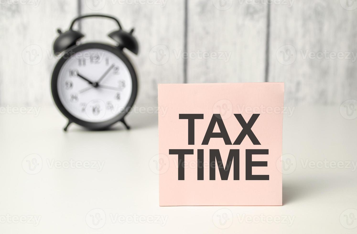 The words TAX TIME on alarm clock and wooden background photo