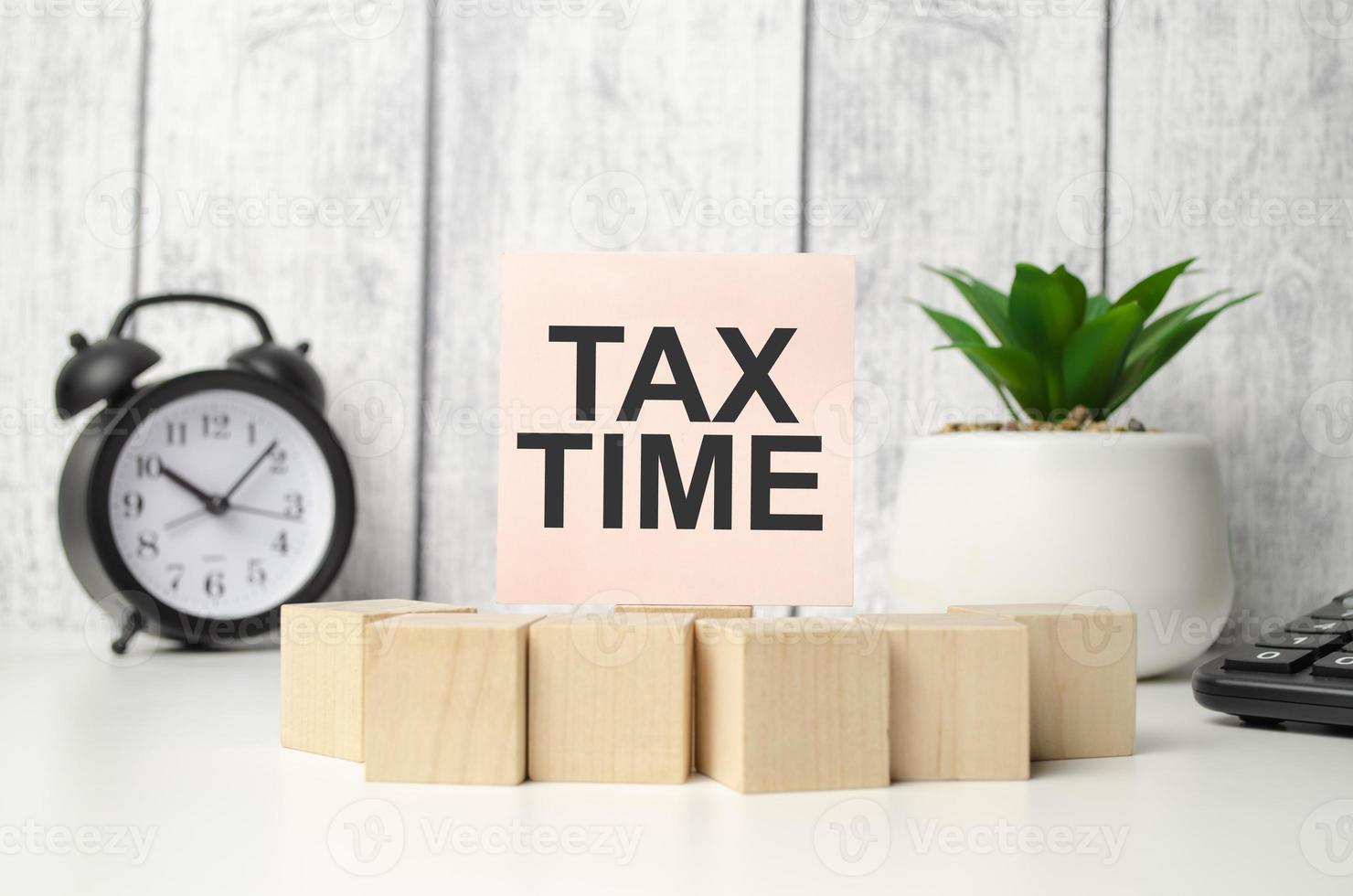 tax time on pink sticker with wooden block and alarm clock photo