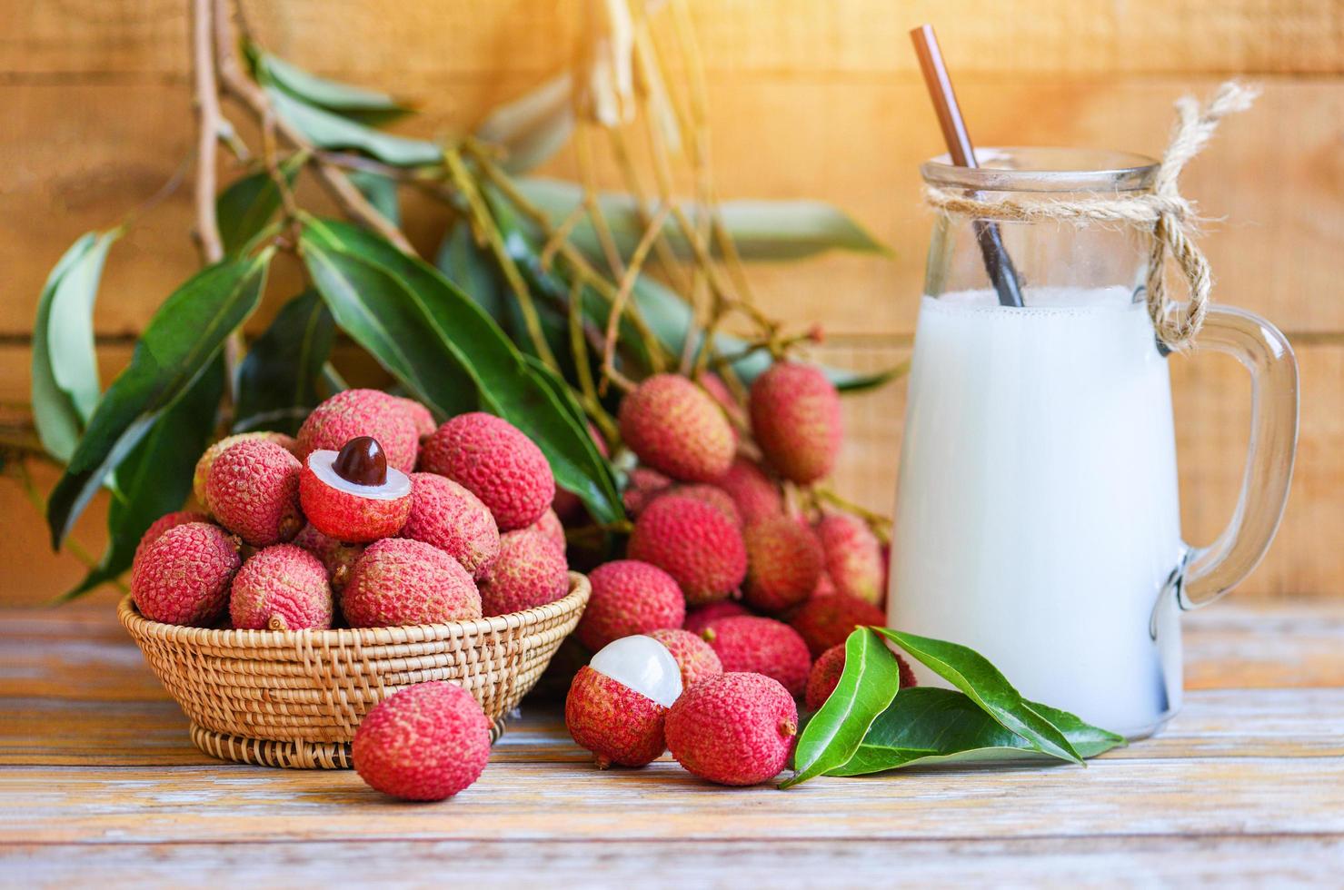 Fresh lychee drink and slice peeled with green leaves harvest in basket from tree tropical fruit summer in Thailand - Lychee juice on wooden table photo