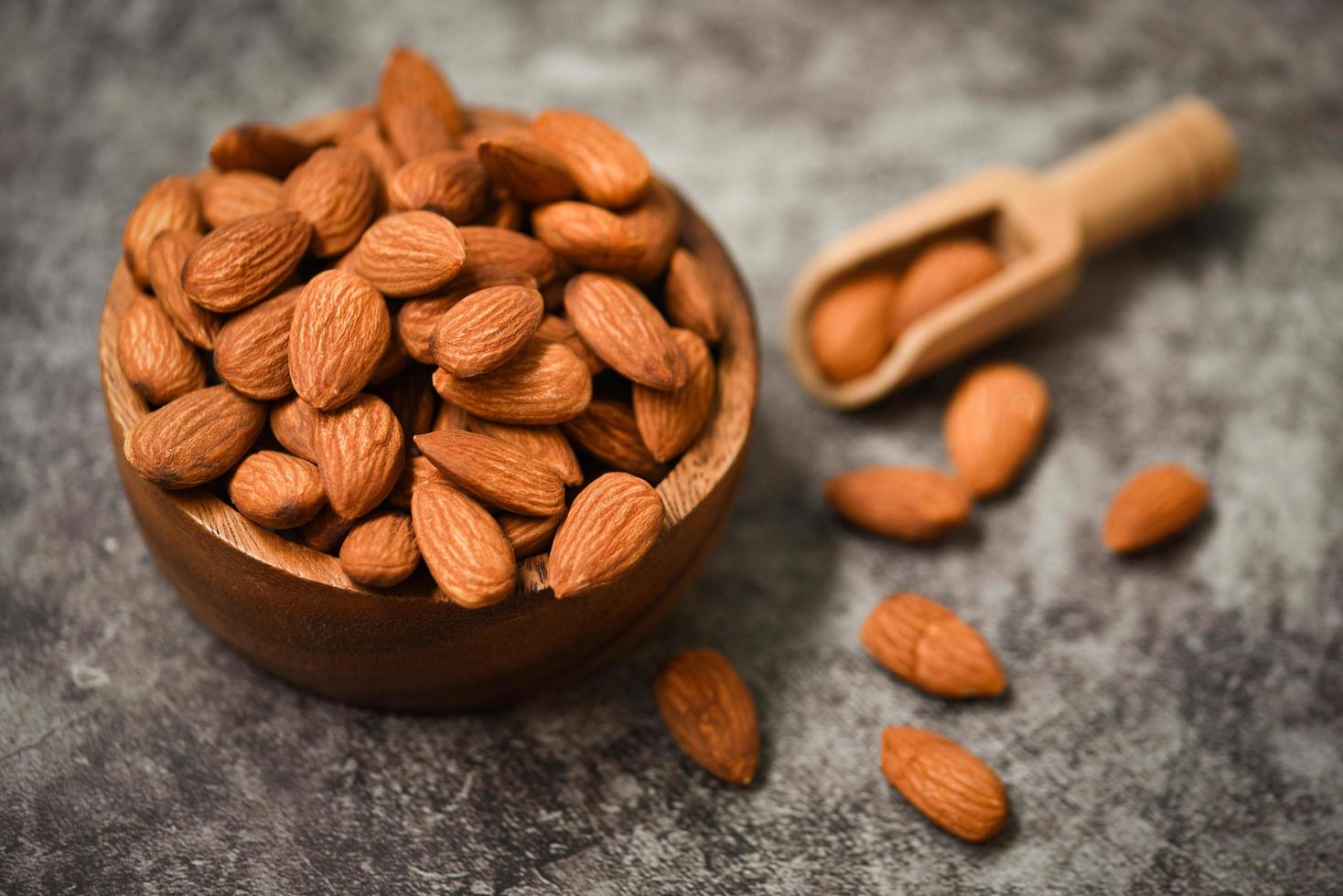 Almonds nuts on wooden bowl on dark background , top view - Roasted almond for snack photo
