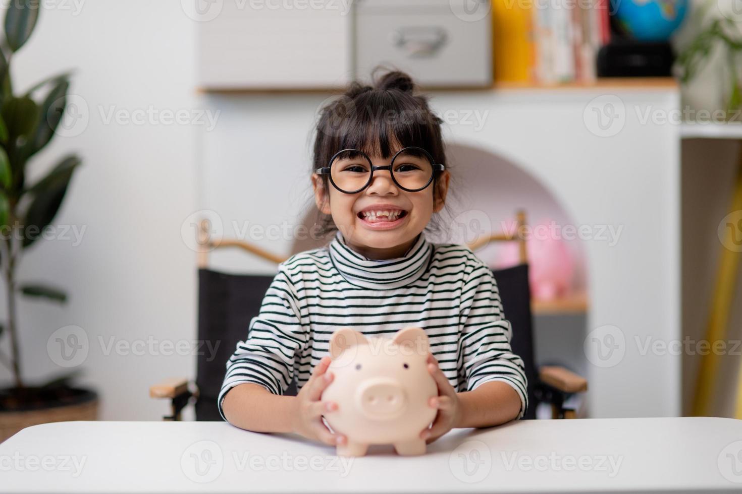 Little Asian girl saving money in a piggy bank, learning about saving, Kid save money for future education. Money, finances, insurance, and people concept photo