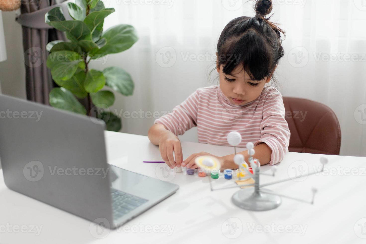 una niña asiática estudia el sistema solar en clase de geografía. mirando el modelo a escala de los planetas foto