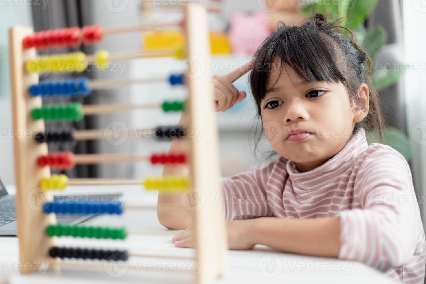 A young cute Asian girl is using the abacus with colored beads to learn how to count at home photo