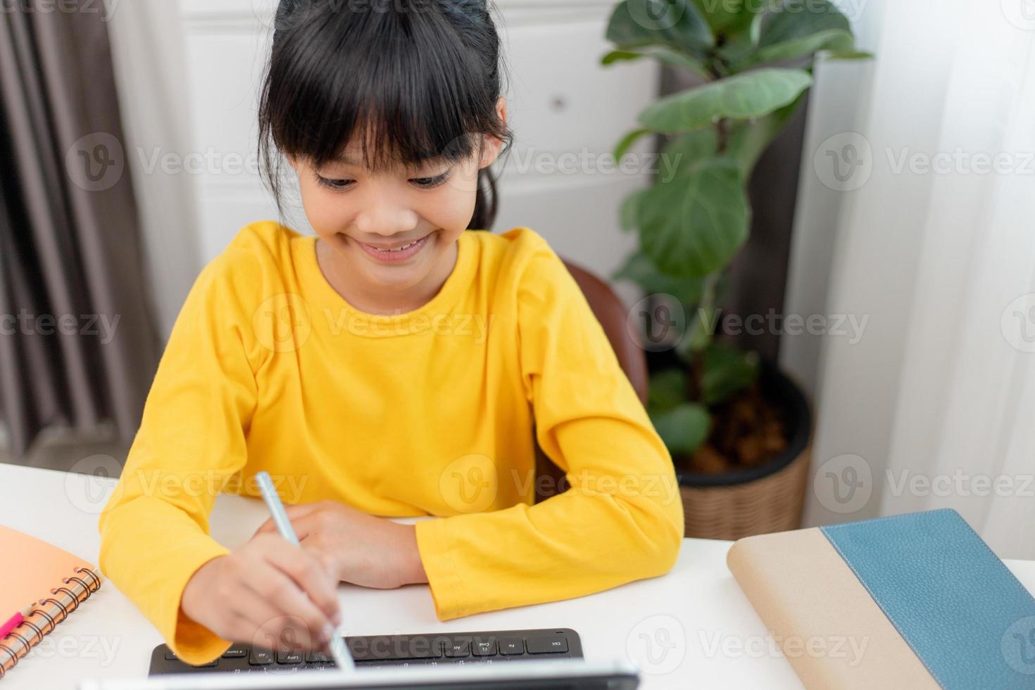 Asian schoolgirl doing her homework with digital tablet at home. Children use gadgets to study. Education and distance learning for kids. Homeschooling during quarantine. Stay at home photo