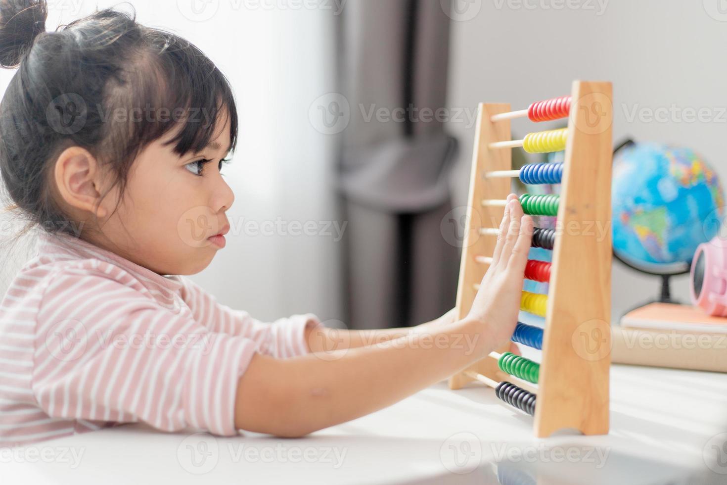 A young cute Asian girl is using the abacus with colored beads to learn how to count at home photo