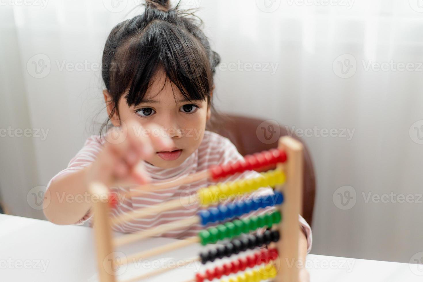 A young cute Asian girl is using the abacus with colored beads to learn how to count at home photo