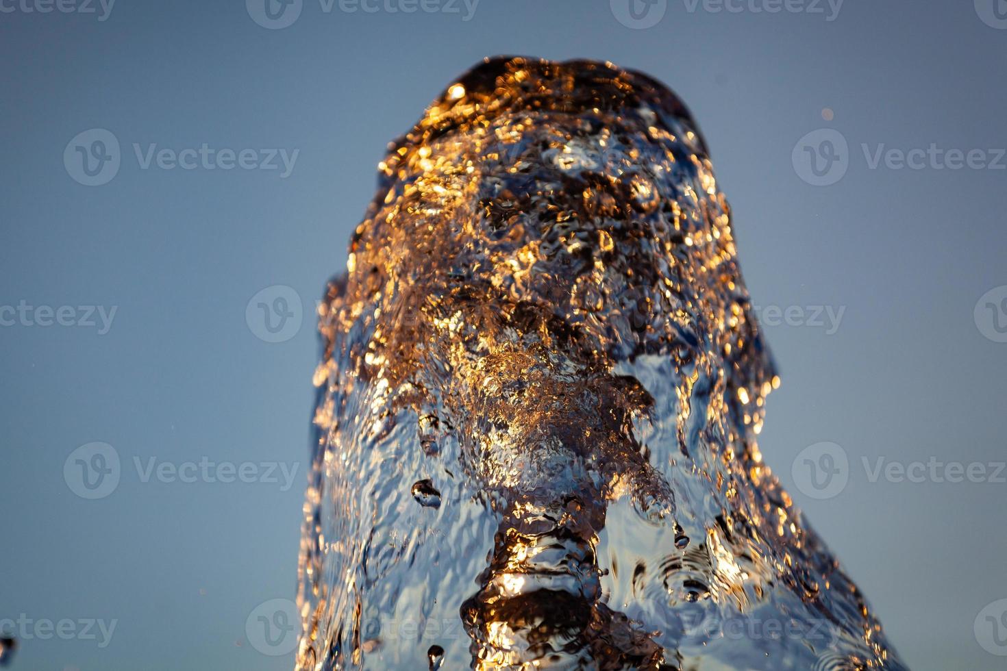 chorros de agua con muchas gotas y burbujas bajo el sol sobre un fondo amarillo anaranjado. un gran plan la textura de las ondas de agua de una gran fuente foto