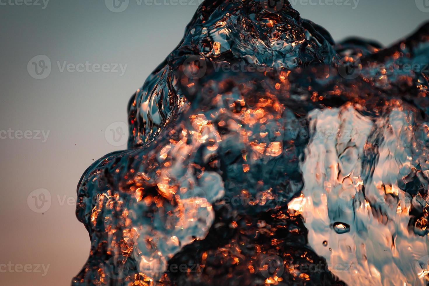 stream of water with droplets and bubbles under the orange and yellow rays of the sun. Texture of water waves of a large fountain photo