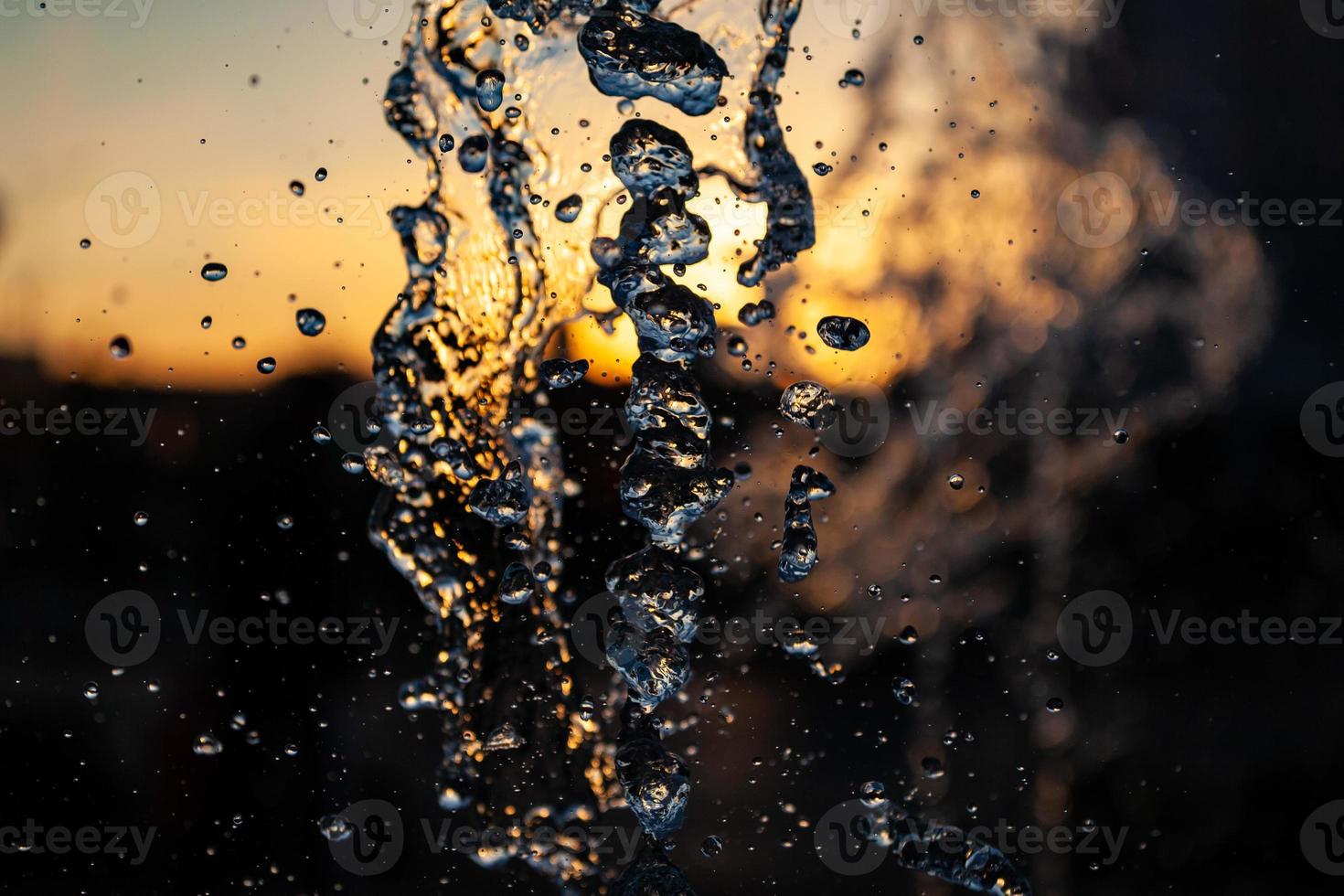 chorros de agua con muchas gotas y burbujas bajo el sol sobre un fondo amarillo anaranjado. un gran plan la textura de las ondas de agua de una gran fuente foto