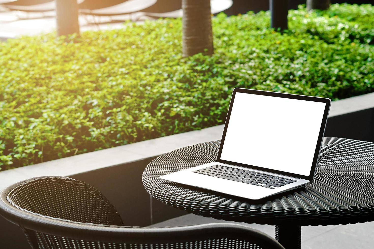 Laptop with blank screen for creative design on the table nearby garden  with sun ray effect. Computer notebook with monitor clipping path for present landing page. Laptop computer mock up template. photo