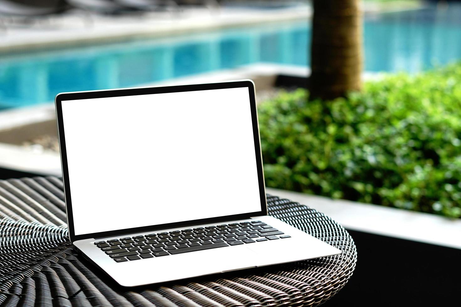 portátil con pantalla en blanco para un diseño creativo en la mesa cerca del fondo de la piscina. computadora portátil con ruta de recorte de monitor para el diseño actual de la página de destino. plantilla de maqueta de computadora portátil foto