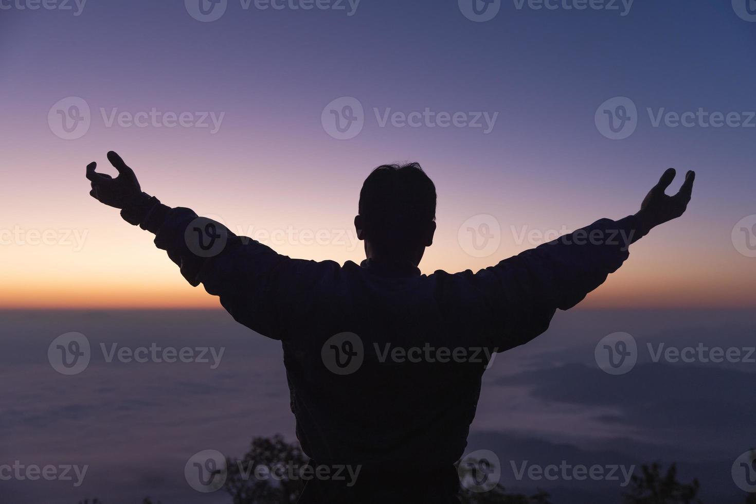 Silhouette of a young man praying to God on the mountain at sunset background.  raising his hands in worship. Christian Religion concept. photo