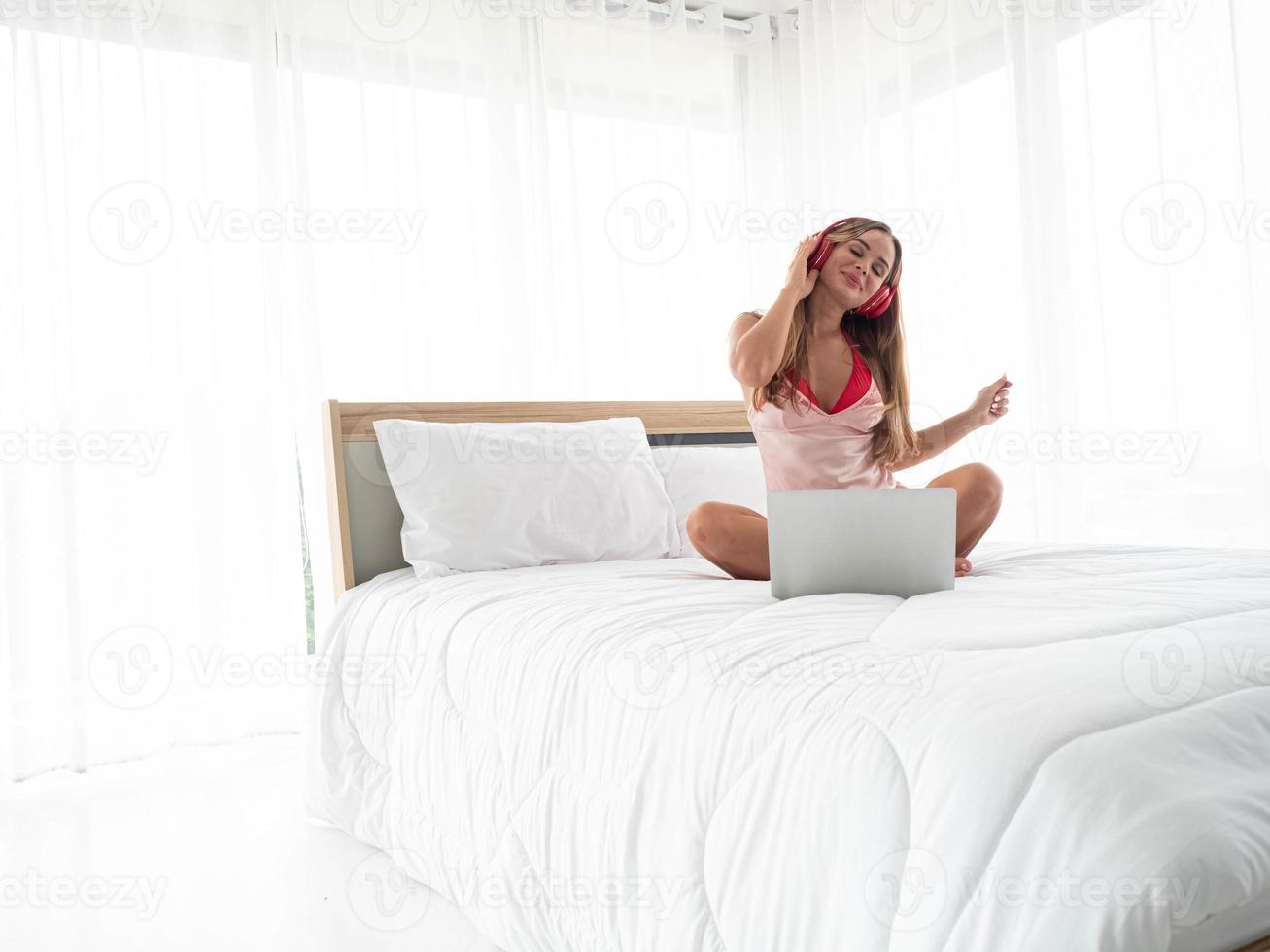 Lady female woman girl her blond hair siting indoor bedroom house studio pillow white isolate background copy space listen music song notebook computer technology headphone relax time person beautiful photo