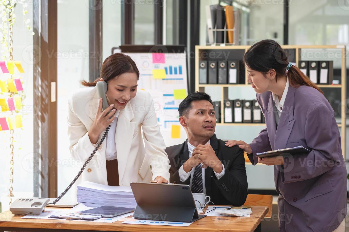 A team of three Asian businessmen is working inside an office where businessmen in black suits are being ordered by their supervisors and bosses a lot causing stress at work. burnout concept photo