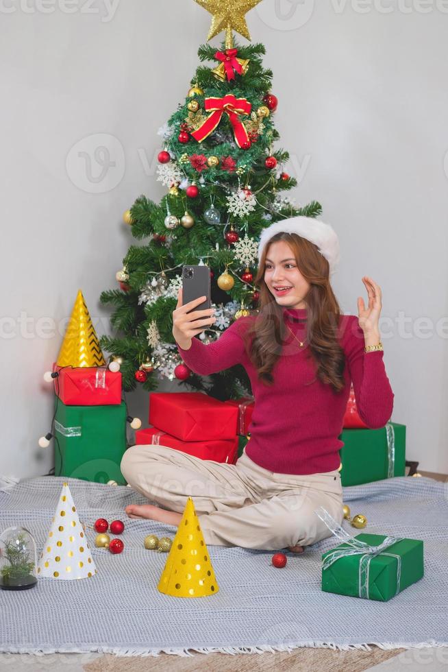 Merry Christmas and Happy Holidays Young woman with a beautiful face in a red shirt shows joy with gift boxes in a house with a Christmas tree decorated with Christmas tree.  Portrait before Xmas photo