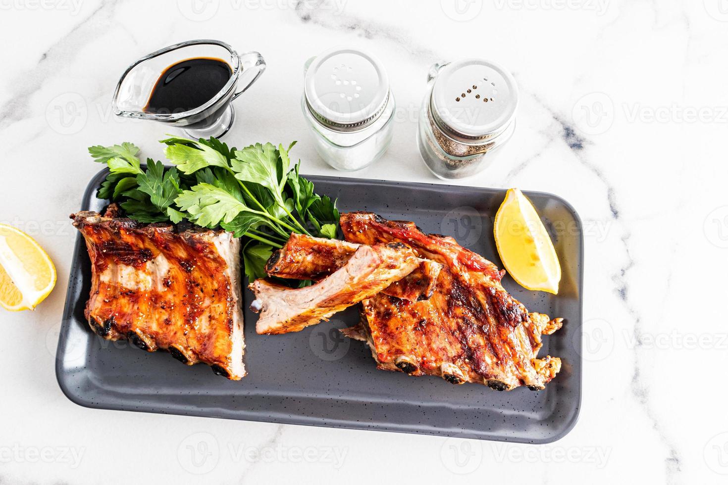 pork ribs grill on a ceramic dark tray with ingredients on a white factual background. exquisite food for barbecue lovers. photo