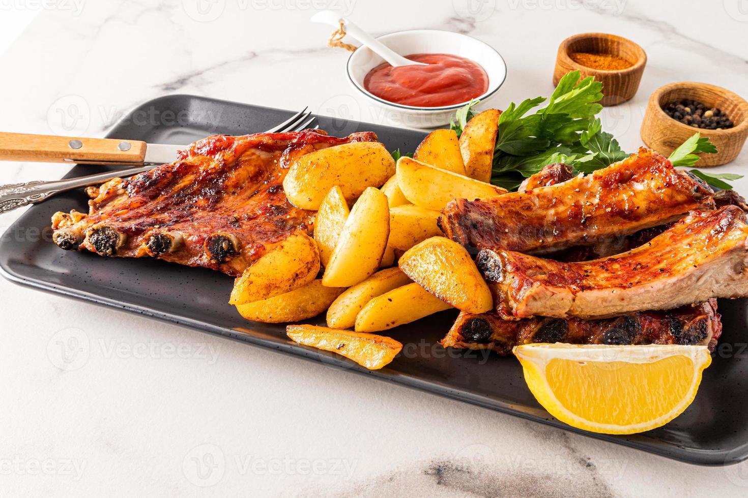 Delicious pork ribs and grilled potato slices served on a ceramic rectangular dish with parsley. the concept of serving the food. menu. photo