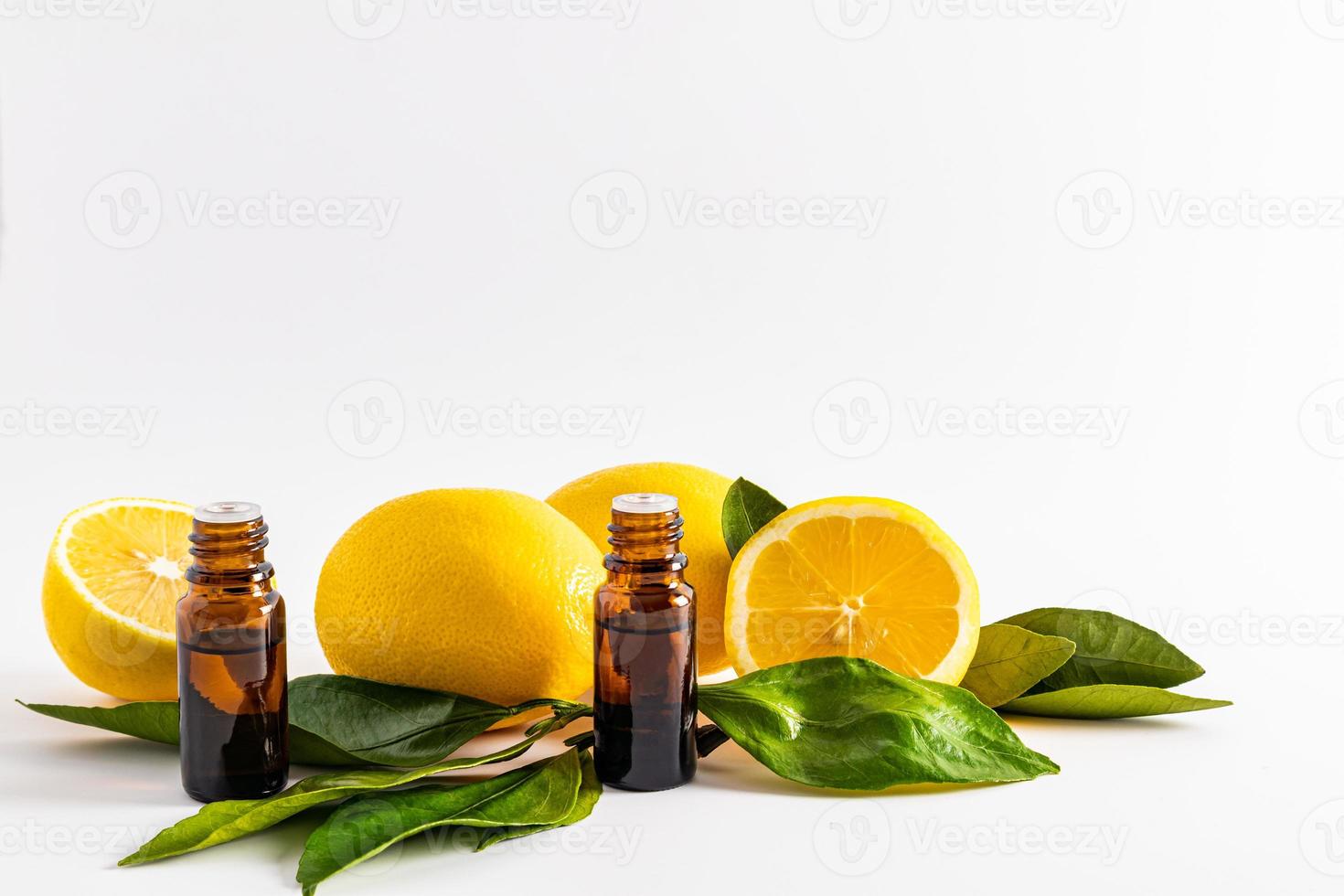 two medical bottles of dark glass with a dropper with lemon essential oil on a white background among ripe fruits and leaves. aromatherapy. photo
