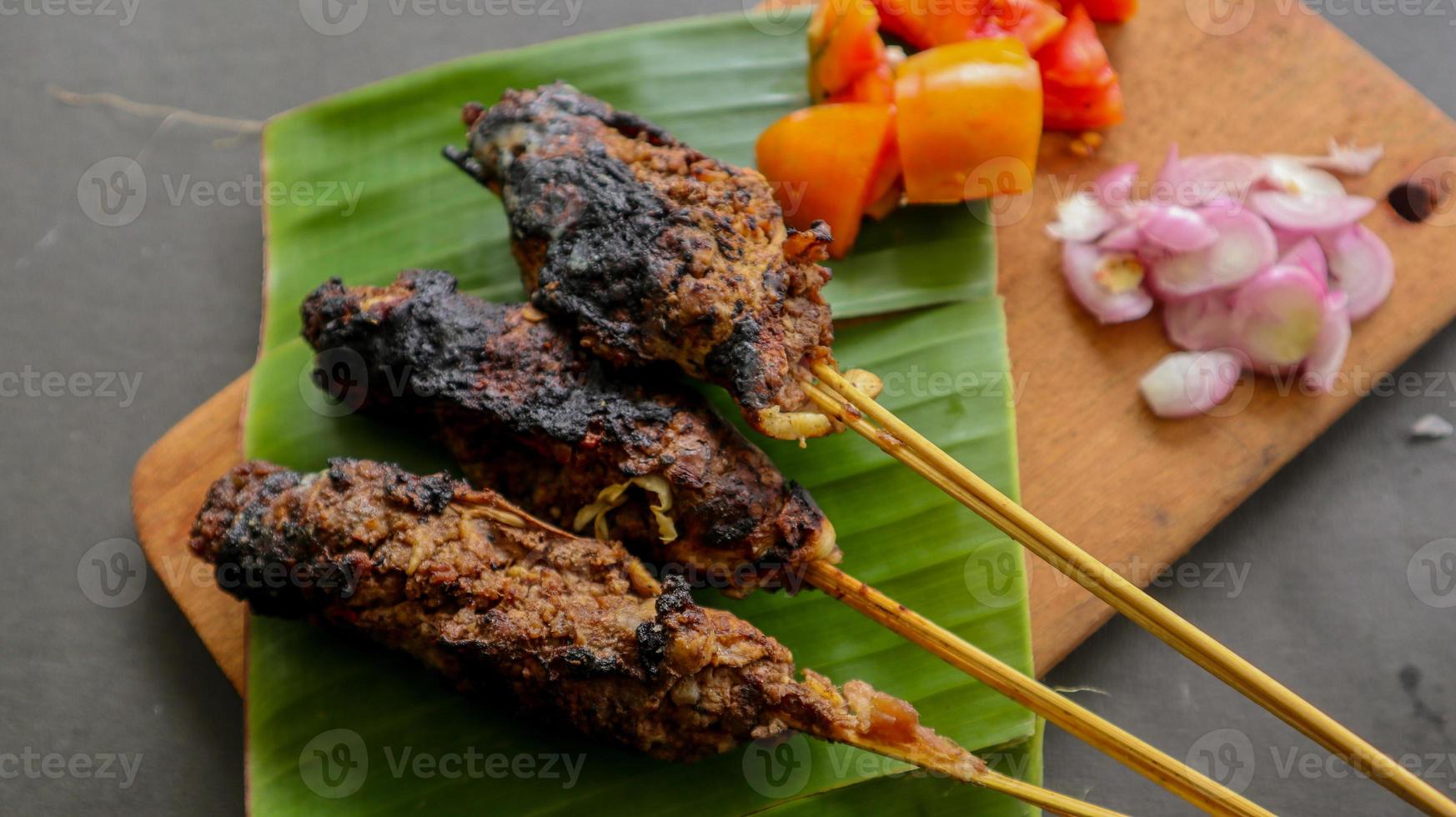 sate buntel o satay buntel es satay hecho de cordero picado envuelto en grasa de cordero y luego asado a la parrilla. condimento con tomates, chalotes, pimienta, repollo foto