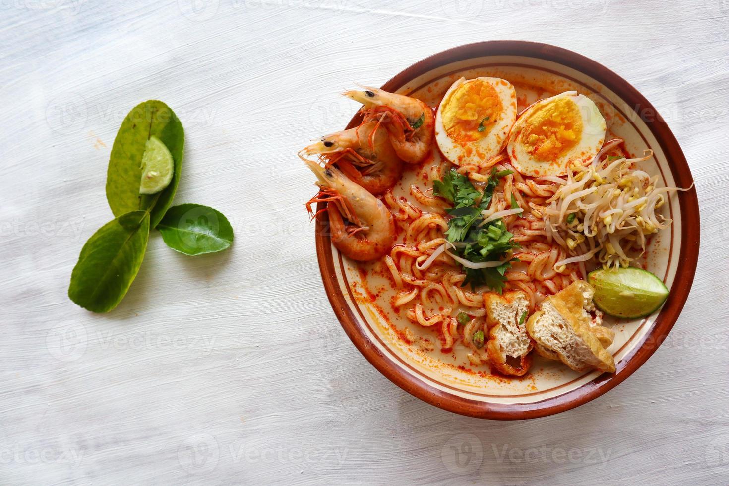 laksa, laksa curry made from vermicelli, noodles, bean sprouts, egg, tofu lime, and shrimp with a spicy soup sauce that is rich in spices. laksa served on bowl, isolated on white background. photo