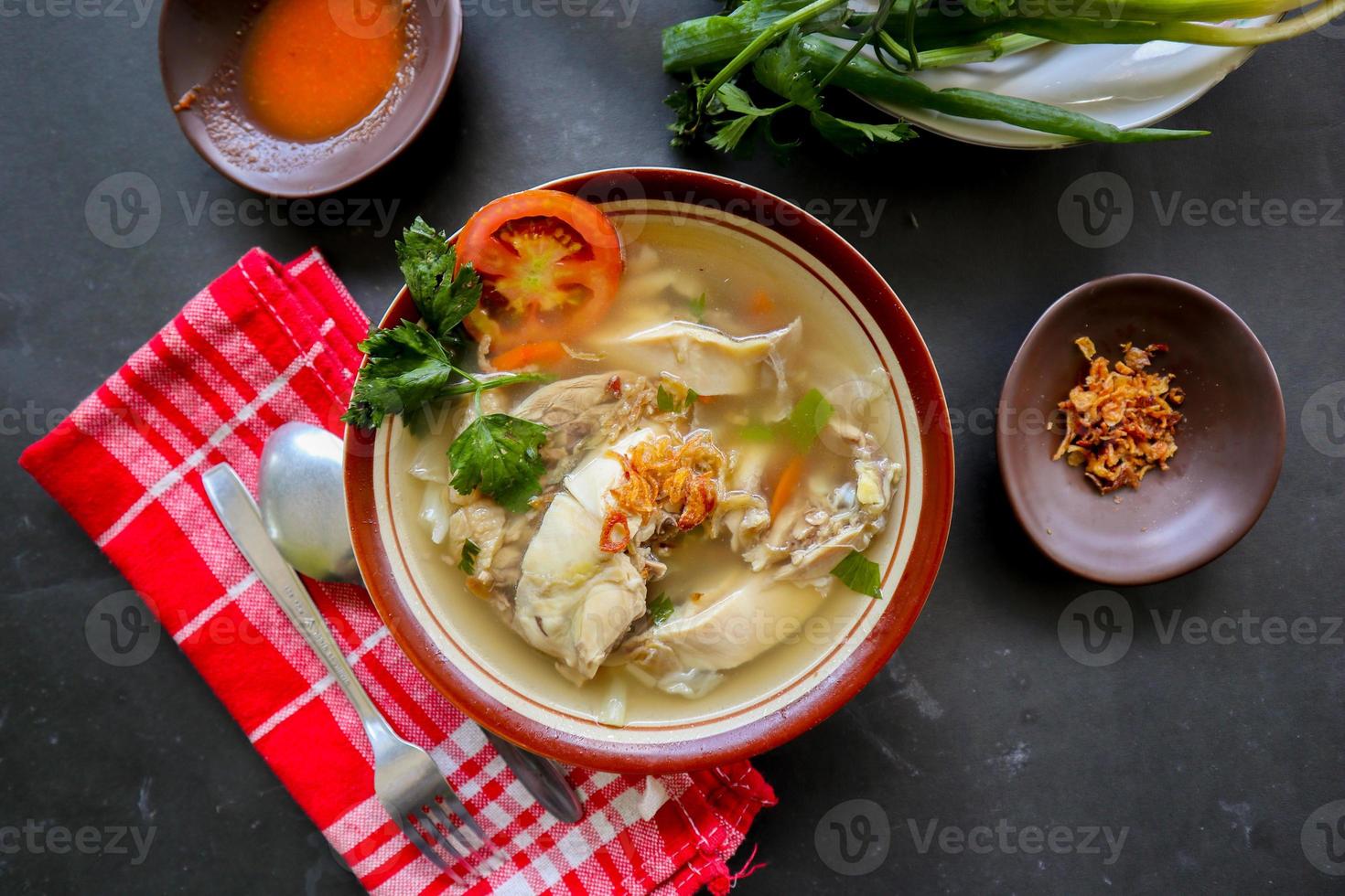 Chicken soup served with vegetables, tomatoes, celery in a bowl, spoon and fork. with black background photo