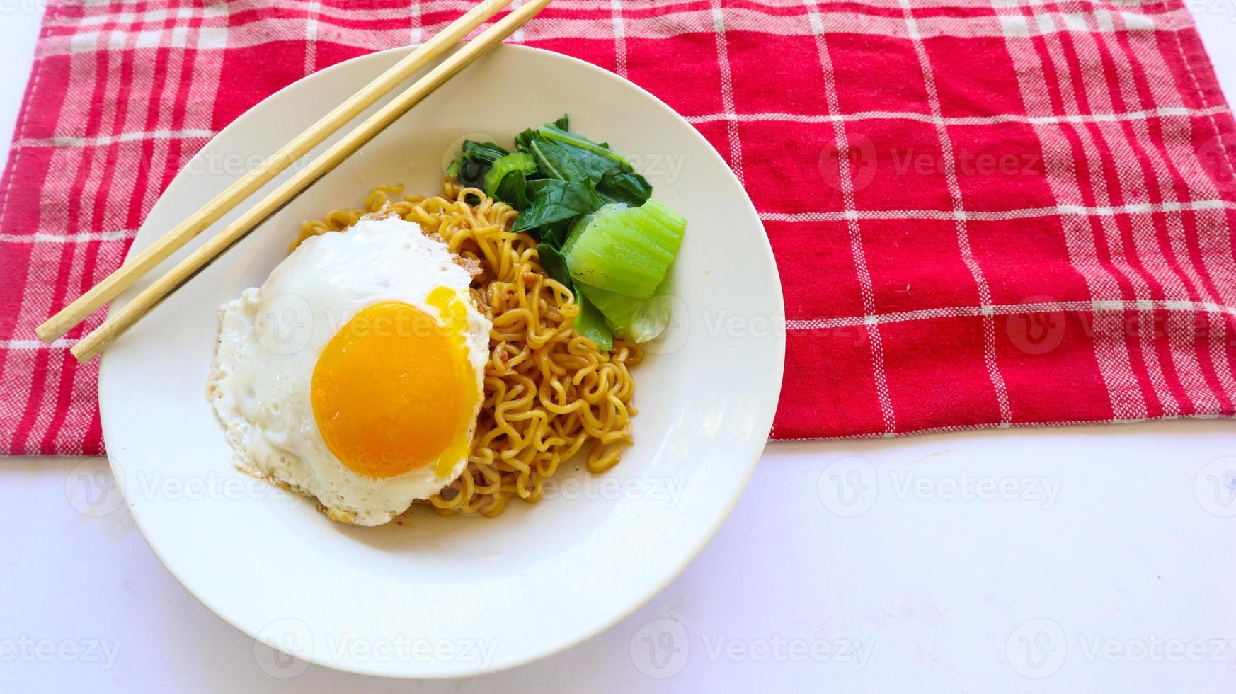 instant noodles served with egg fried and mustard greens on plate. instant fried noodle indomie photo