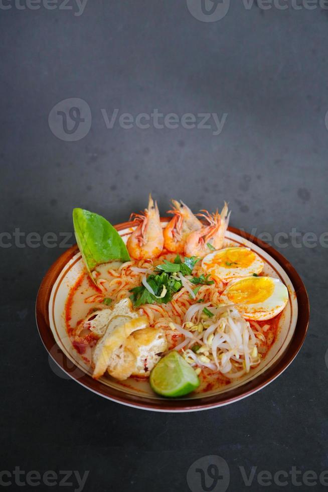 laksa, laksa curry made from vermicelli, noodles, bean sprouts, egg, tofu lime, and shrimp with a spicy soup sauce that is rich in spices. laksa served on bowl, isolated on white background. photo