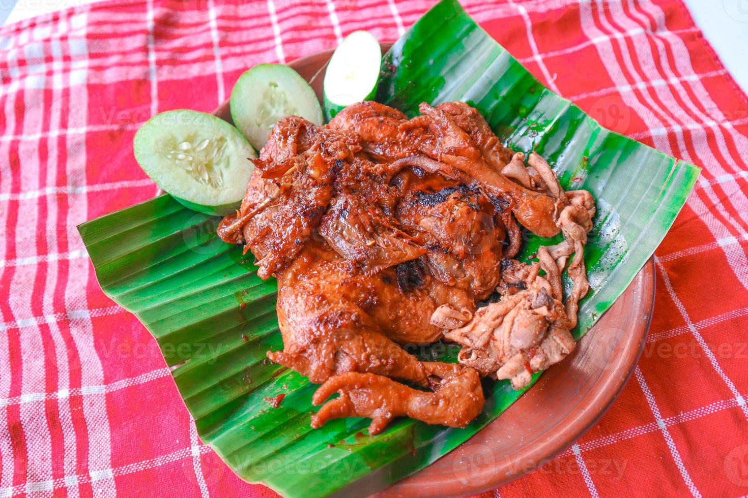 grilled chicken or ayam bakar with cucumber slash served on banana leaf and plate. ayam bakar is traditional grilled chicken from indonesia photo