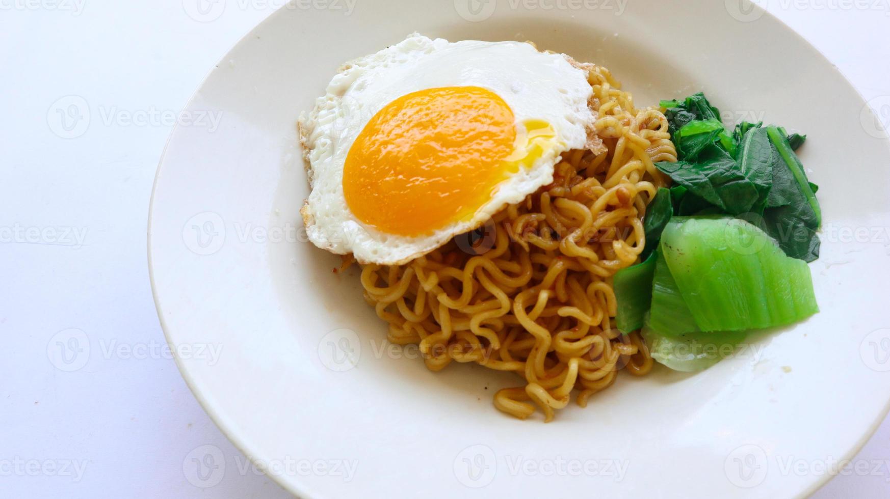 instant noodles served with egg fried and mustard greens on plate. instant fried noodle indomie photo