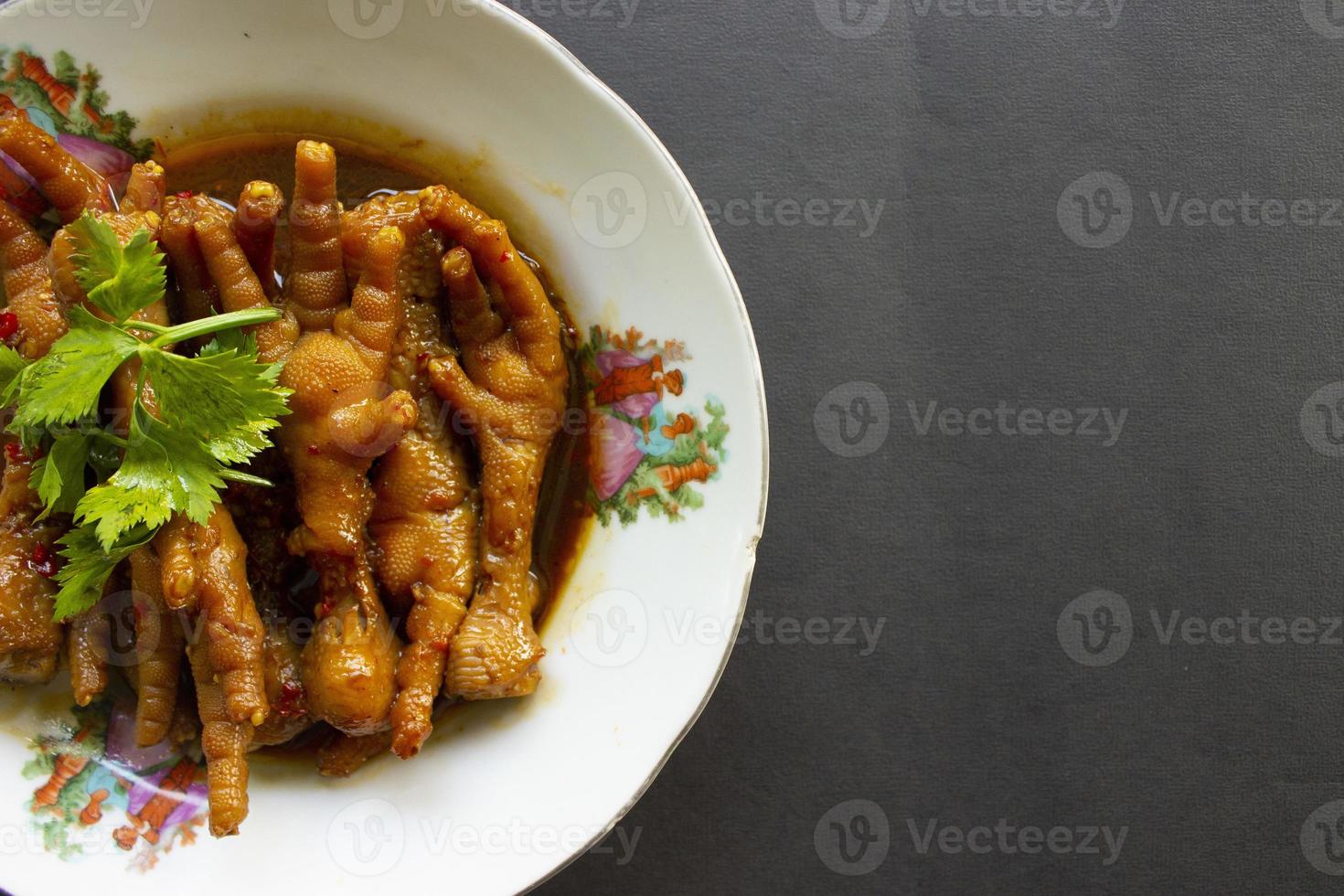Spicy chicken feet with celery, chili, onion, garlic served with a white plate isolated from a black background. photo