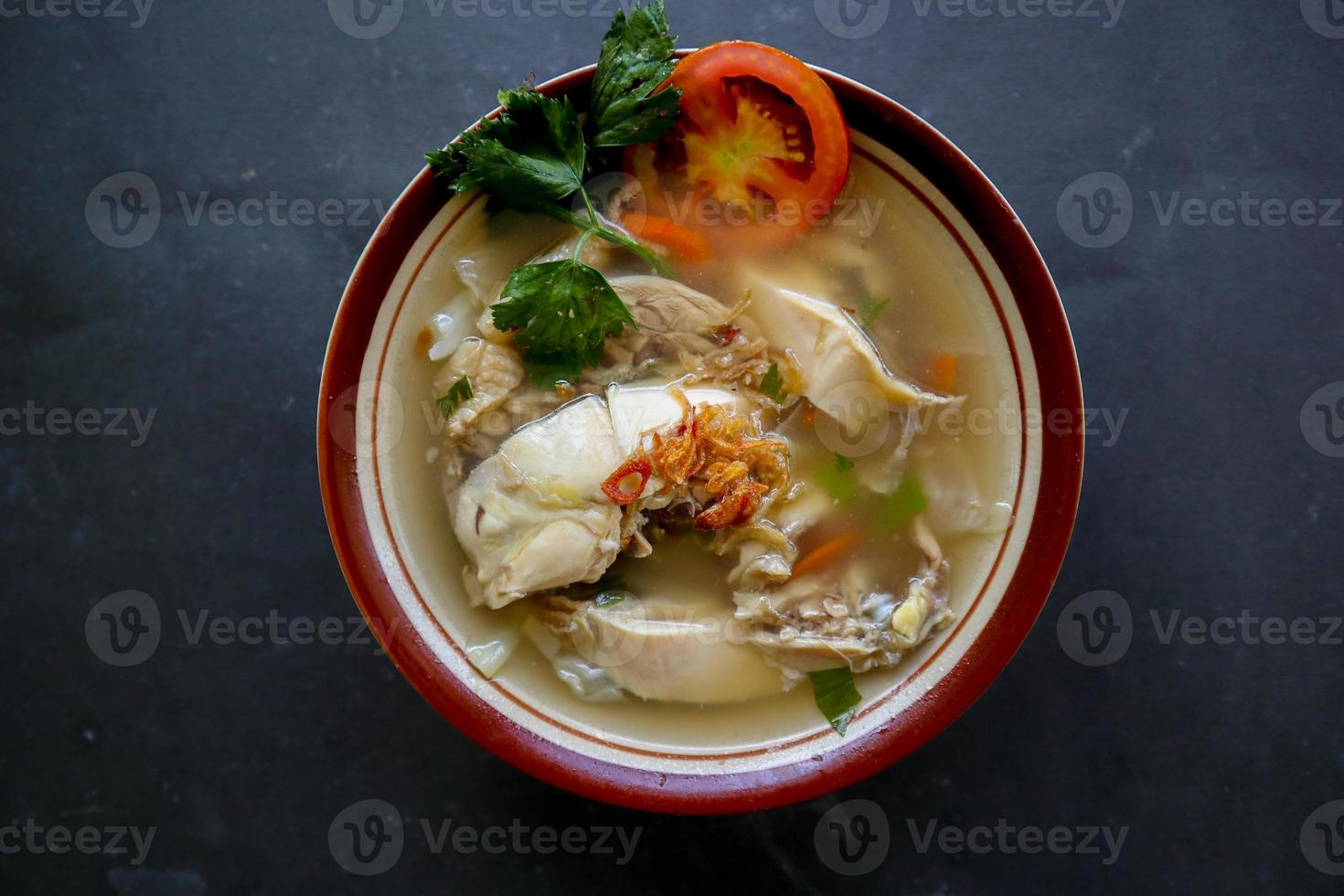 Chicken soup served with vegetables, tomatoes, celery in a bowl, spoon and fork. with black background photo