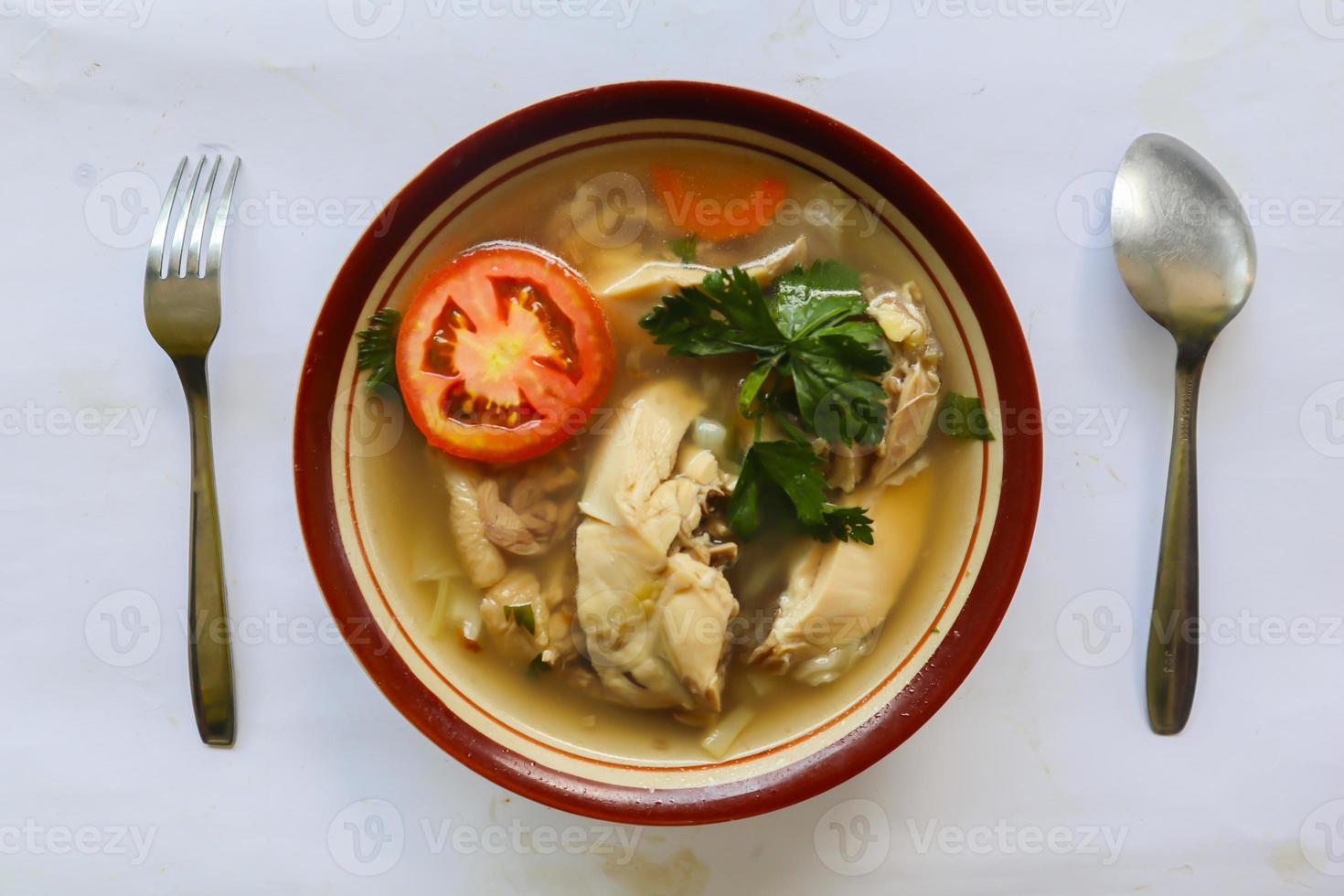 Chicken soup served with vegetables, tomatoes, celery in a bowl, spoon and fork. with black background photo