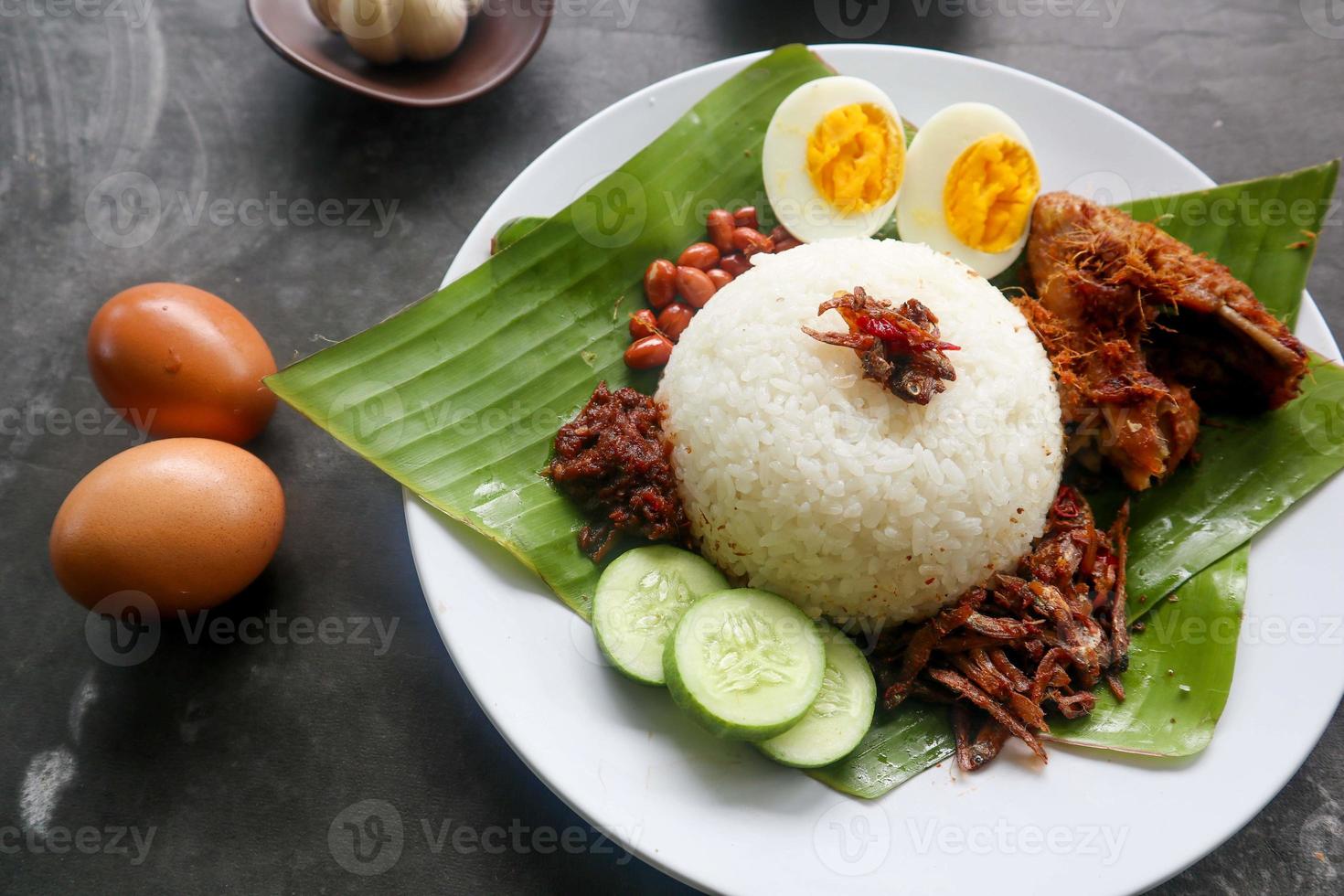 nasi lemak, is traditional malay made boiled eggs, beans, anchovies, chili sauce, cucumber. from dish served on a banana leaf photo