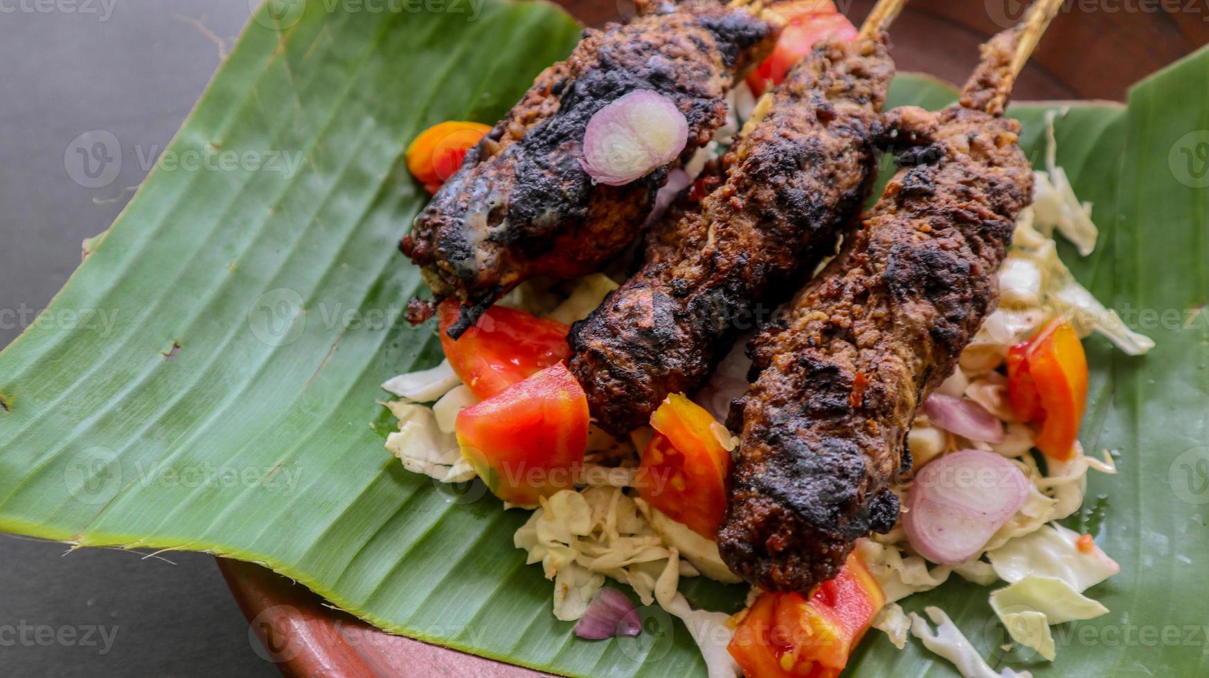 sate buntel o satay buntel es satay hecho de cordero picado envuelto en grasa de cordero y luego asado a la parrilla. condimento con tomates, chalotes, pimienta, repollo foto