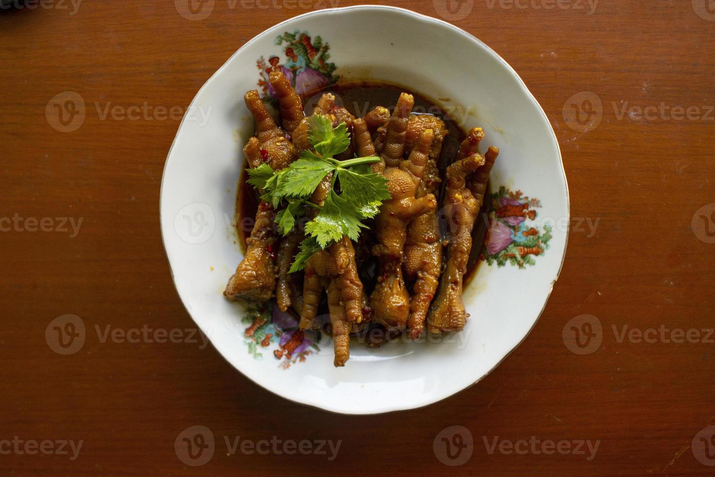 Spicy chicken feet with celery, chili, onion, garlic served with a white plate isolated from a black background. photo