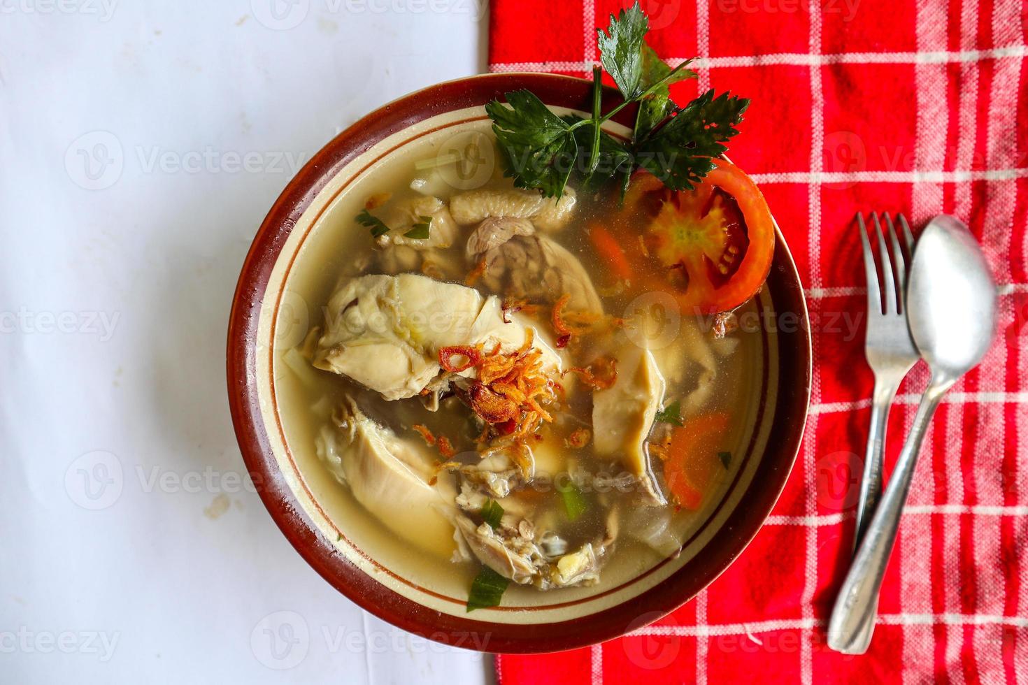 Chicken soup served with vegetables, tomatoes, celery in a bowl, spoon and fork. with black background photo