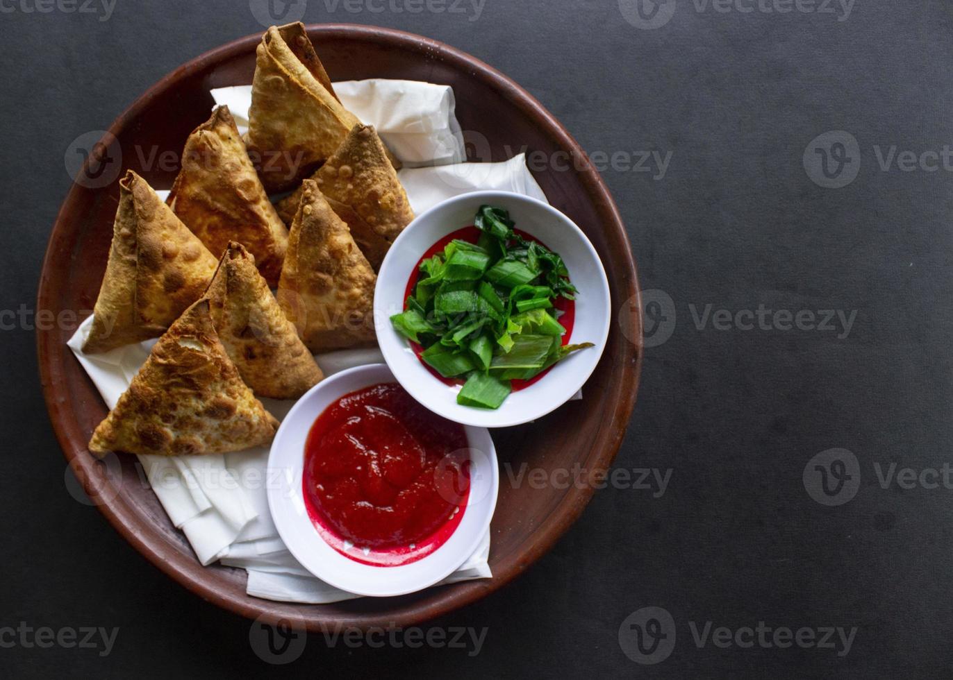 Samosa, samsa or somsa are triangular fried pastries or pastri served with tomato sauce and leek slice, on black background photo