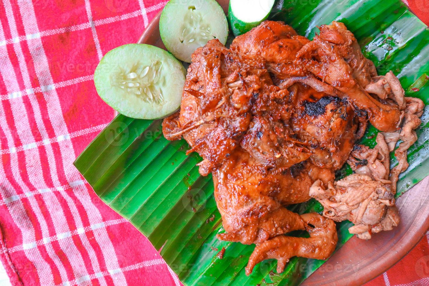grilled chicken or ayam bakar with cucumber slash served on banana leaf and plate. ayam bakar is traditional grilled chicken from indonesia photo